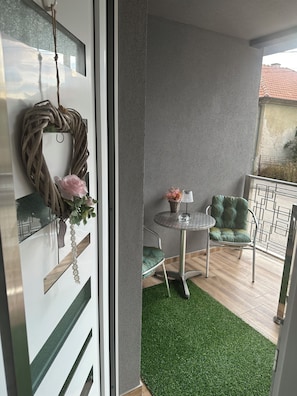 A balcony with a round table, two chairs, a small potted plant, and a decorative wreath.