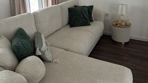 A living room with a beige sofa, a round side table, a mirror, and a window with curtains. - La Luna 2
Modern Haus im Stadzentrum (Zaječar)