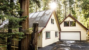 Ein zweigeschossiges Haus mit Garage, umgeben von hohen Bäumen und einer Holzterrasse.