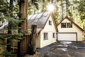 Ein zweigeschossiges Haus mit Garage, umgeben von hohen Bäumen und einer Holzterrasse.
