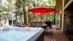 Ein Whirlpool auf einer Holzterrasse, umgeben von Stühlen und einem roten Sonnenschirm.