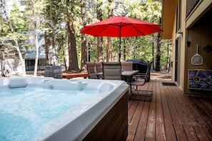Ein Whirlpool auf einer Holzterrasse, umgeben von Stühlen und einem roten Sonnenschirm.