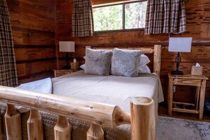 A wooden cabin bedroom with a bed, two bedside tables, a window, and plaid curtains. - Two Incredible Cabins for a Memorable Family Getaway in Dorrington, California (Dorrington)