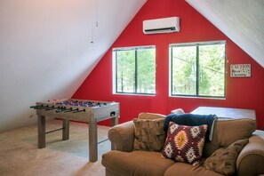 A room with a foosball table, a couch with patterned cushions, and two windows with a view of greenery. - Two Incredible Cabins for a Memorable Family Getaway in Dorrington, California (Dorrington)