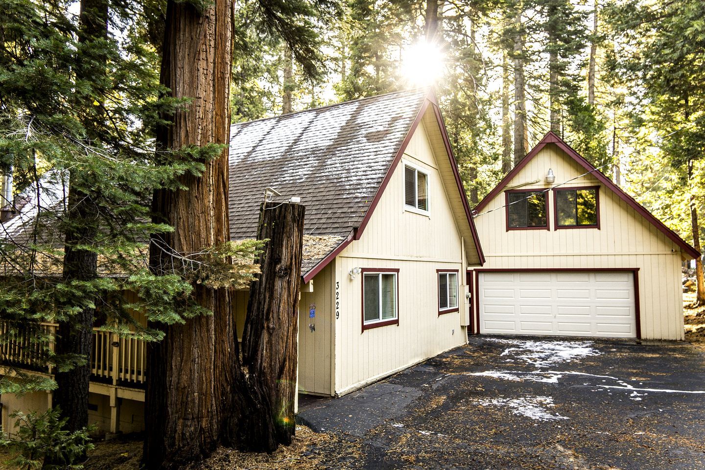 Une maison à deux étages avec un garage, entourée de grands arbres et dotée d’une terrasse en bois.