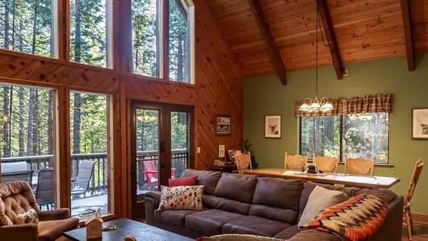 Ein gemütliches Blockhaushaus-Interieur mit einer großen Holzbalkendecke, einem Essbereich mit Tisch und Stühlen sowie einer Sitzecke mit einer Couch und Sesseln.