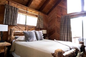Ein schlicht eingerichtetes Schlafzimmer im Chalet-Stil mit einem Bett, zwei Kissen, einem Nachttisch mit Lampe und Karo-Vorhängen.