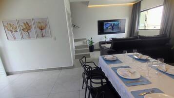 Un coin repas avec une table dressée pour quatre personnes, un téléviseur à écran plat fixé au mur et un escalier menant à l’étage supérieur.