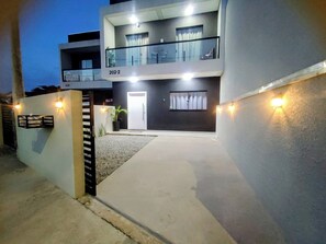 A modern two-story building with a balcony, a door, and a small garden area. - New, cozy 3-bedroom townhouse near the sea and the center of Matinhos. (Matinhos)