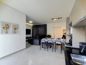 A modern living room with a dining area, a flat-screen TV mounted on the wall, and a dining table set for six. - New, cozy 3-bedroom townhouse near the sea and the center of Matinhos. (Matinhos)