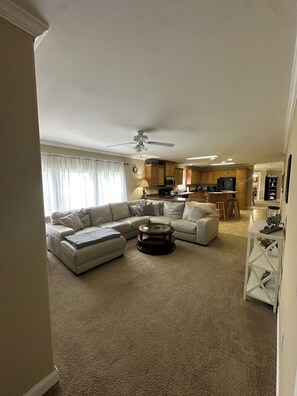 Ein Wohnzimmer mit Ecksofa, Couchtisch und einer Küche im Hintergrund.