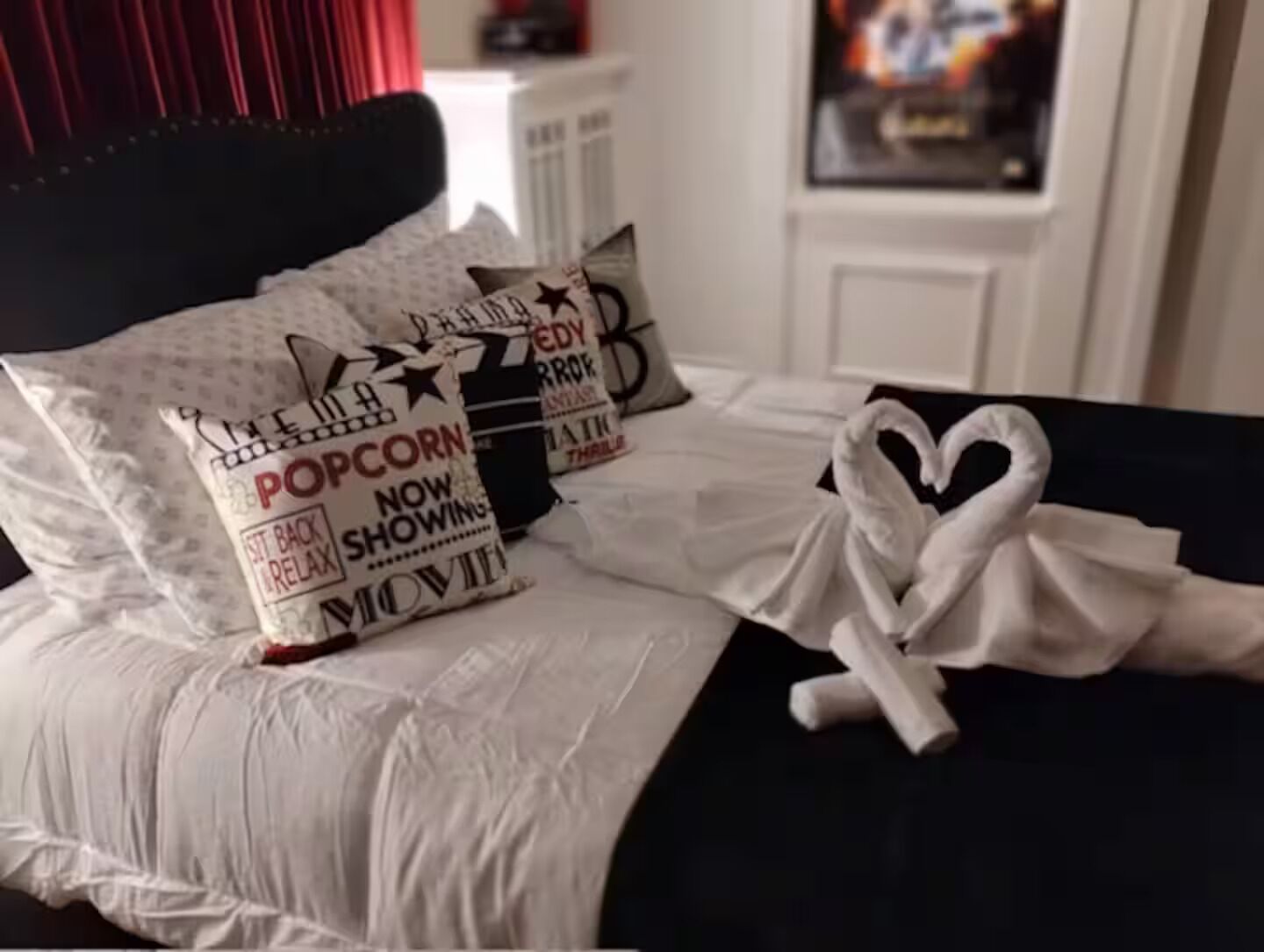 Ein Bett mit weißer Bettwäsche, einem schwarzen Kopfteil und Kissen mit Film-Motiven.