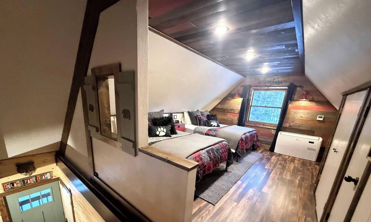 A loft bedroom with a sloped ceiling, wooden beams, and a window providing natural light.