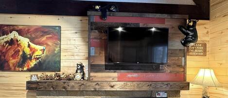 A room with a mounted flat-screen TV, wooden wall paneling, a bear statue, and a painting of a roaring animal.