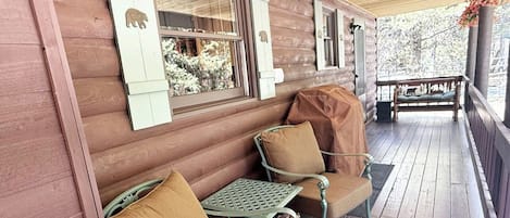 Una cabaña de madera con un porche, dos sillas con cojines, una mesita y un banco.