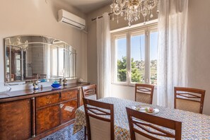 Ein Essbereich mit Tisch, Stühlen, einer Kristallleuchter, einem großen Spiegel und einem Fenster mit Blick.