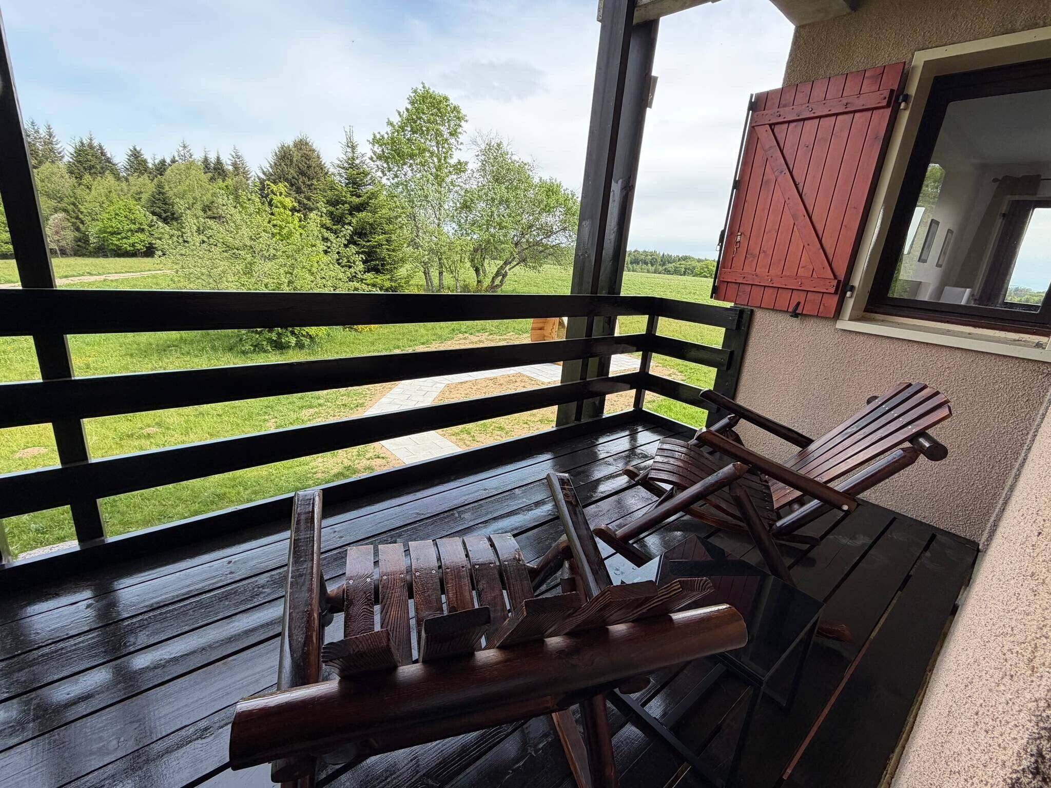 En træterrasse med bænk og stol, en rød lukket markise, samt udsigt over et gr ønt landskab.
