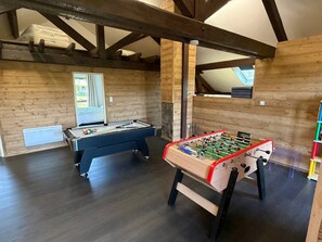 Una habitación con mesa de billar, mesa de futbolín, paredes de madera y una ventana.