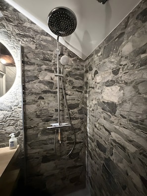 A shower with a handheld showerhead and a wall-mounted rain showerhead, set against a stone wall backdrop.