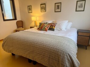 Una cama bien hecha con un edredón estampado, una lámpara de noche y una silla.