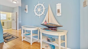 A room with a nautical theme, featuring a sailboat model, a ship's wheel, and a small shelf with decorative items.