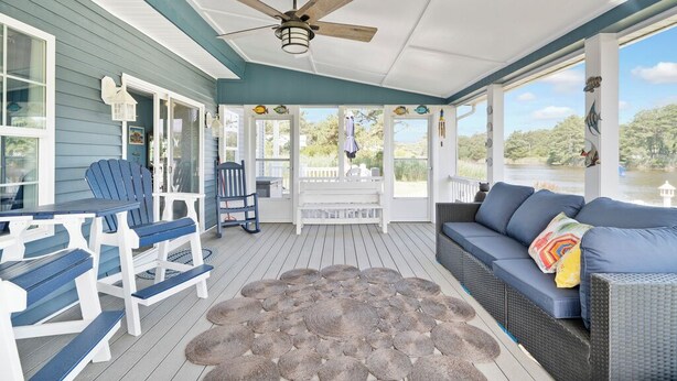 A covered porch with a ceiling fan, seating area, and a view of the water.