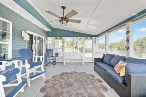 Eine überdachte Veranda mit Deckenventilator, einer Sitzgelegenheit und Blick auf das Wasser.