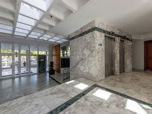 Eine Lobby mit Marmorboden, einer Rezeption, einem Blumentopf und einem Aufzug.