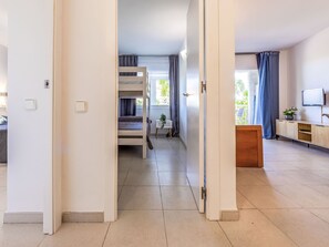 A modern apartment with a bunk bed, a small table with a plant, a TV on a wooden cabinet, and a view of the outdoors. - Apartment Royal by Interhome (Salou)
