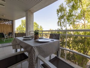 An outdoor dining area with a table set for two, chairs, and a view of trees and buildings. - Apartment Royal by Interhome (Salou)