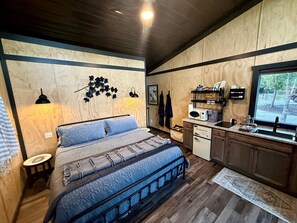 A bedroom with a bed, a small bedside table, a wall-mounted lamp, and a window with a view of trees. - Scenic Studio Chalet with Panoramic Brow Views & Outdoor Shower near Cloudland Canyon, Menlo, Georgia (Menlo)