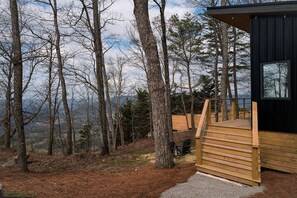 Eine Holzhütte mit einer Holzdielenveranda und schwarzem Anstrich, umgeben von Bäumen und einer Berglandschaft.