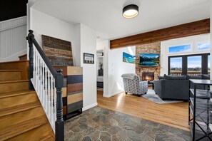 Eine Treppe mit Holzbodenstufen und weißen Geländern, ein fußbodenböden mit Steinmuster, ein Kamin mit Steinverkleidung, ein graues Sofa und ein Ausblick durch ein Fenster.