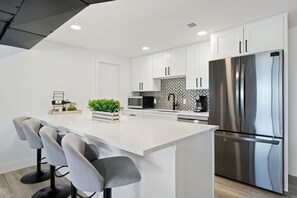 Una cocina moderna con armarios blancos, un refrigerador de acero inoxidable y una isla central con taburetes de bar.