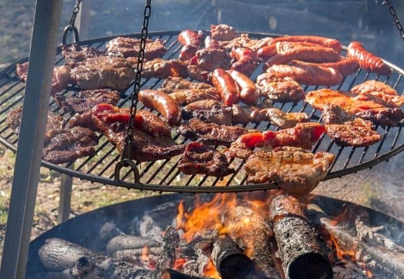 Una parrilla con diversos tipos de carne asándose sobre fuego abierto.