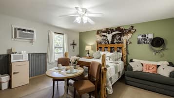 A compact room with a bed, a dining table, a chair, a microwave, a dresser, and a ceiling fan.