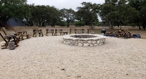 Un área de grava con sillas y bancos de madera dispuestos alrededor de un pozo de fuego de piedra.