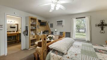 A bedroom with a bed, a desk, a chair, a ceiling fan, a window, and a view of the outdoors.
