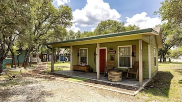 Une petite maison de plain-pied avec un porche, une porte rouge et une enseigne sur laquelle on peut lire « RANCHER ».