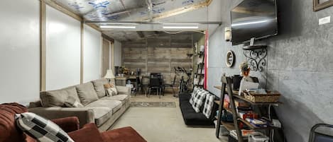 A living room with a sofa, a coffee table, a TV mounted on the wall, and a bicycle in the background.