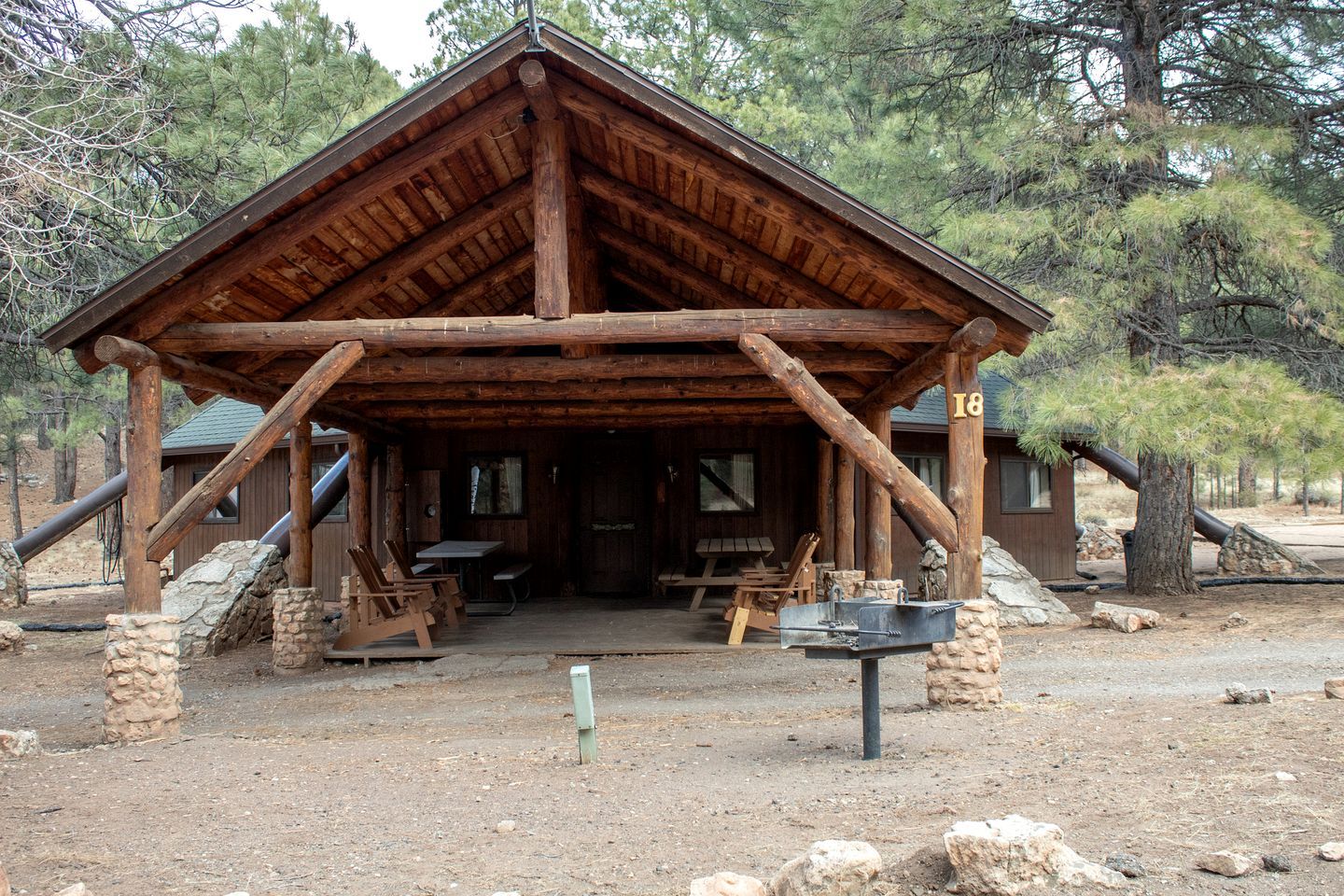 A rustic wooden cabin with a pitched roof, stone pillars, and a number '18' sign.