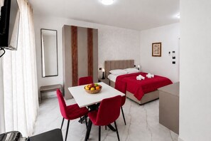 Ein Hotelzimmer mit einem Bett, einem Tisch mit Stühlen, einer Obstschale, einem Fernseher und einem Spiegel.