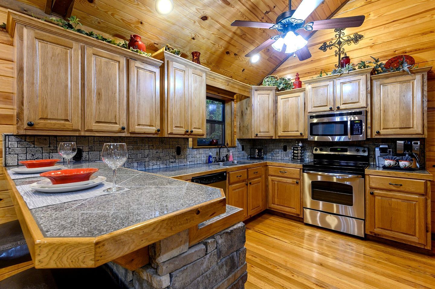 Una cocina con armarios de madera, encimeras de granito, una isla de piedra, electrodomésticos de acero inoxidable y un ventilador de techo.