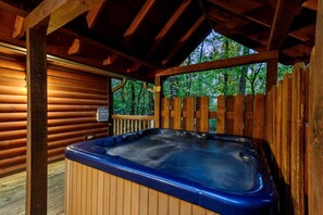 Eine Holzterrasse mit Whirlpool, Holzwertungen und Blick auf Bäume.
