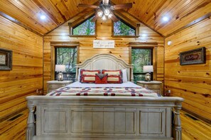 Ein Schlafzimmer mit Holzwandverkleidung, einem großen Bett, zwei Nachttischlampen und einem Deckenventilator.
