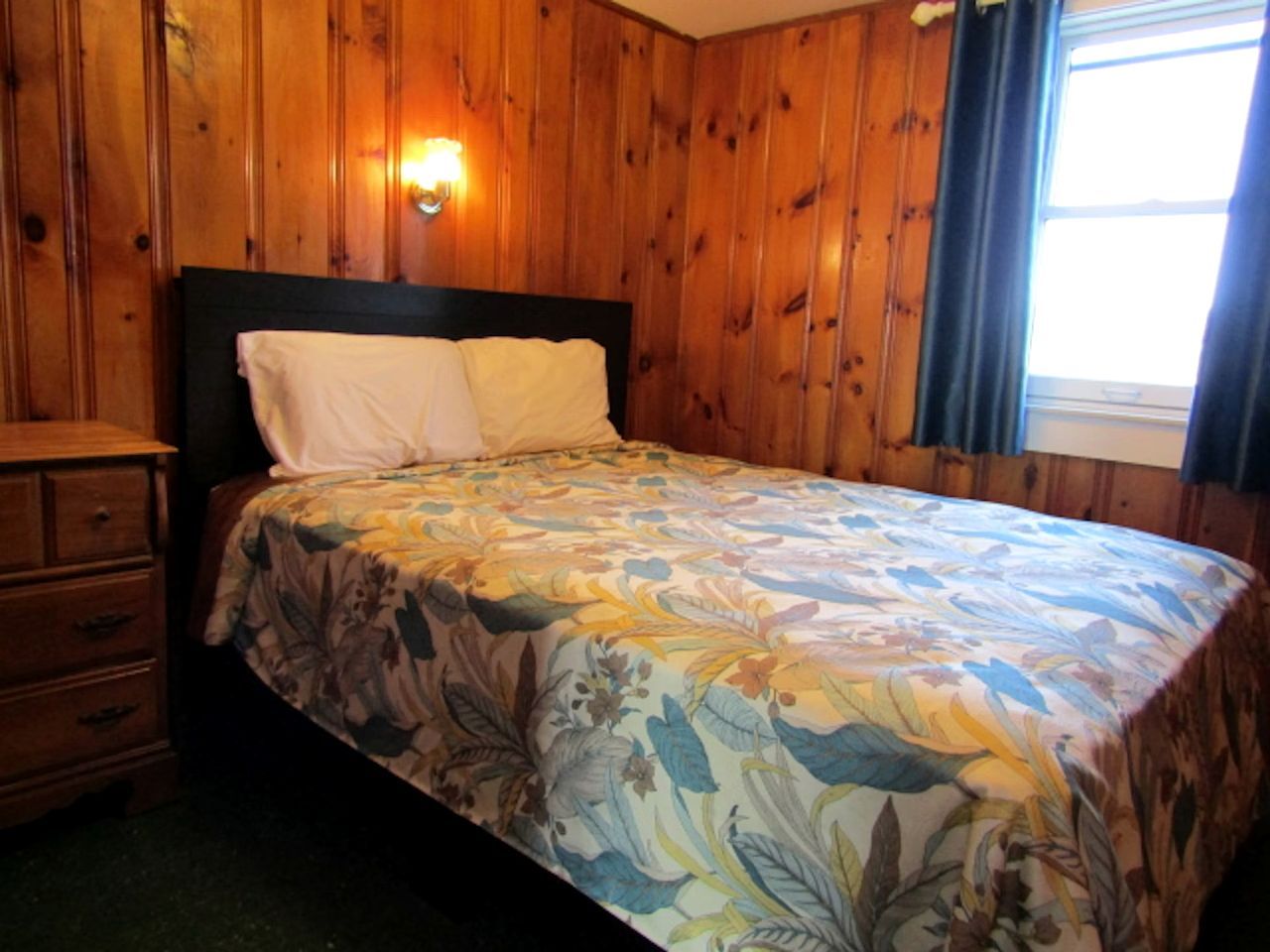 A wooden-paneled room with a bed, a nightstand, and a dresser.