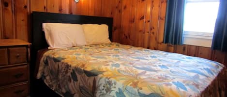 Una stanza con rivestimenti in legno, un letto, un comodino e una cassettiera.