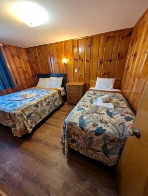 A room with two beds, wooden walls, a nightstand, and a wall-mounted light. - Oceanfront Sanctuary with Elevated Coastal Comfort in North Truro, Massachusetts (North Truro)