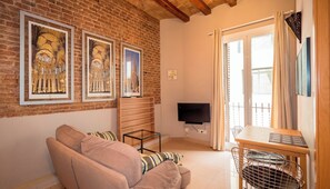 Ein Wohnzimmer mit Backsteinwand, einer Couch, einem Fernseher, einem Tisch und einem Fenster mit Vorhängen.