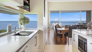 Una cocina moderna con vista al mar, un comedor con mesa y sillas, y un ventanal grande.